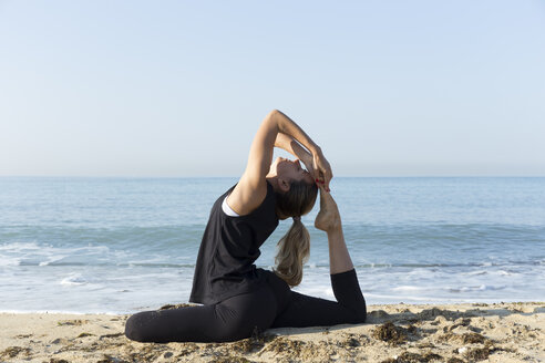 Young woman practicing yoga on the beach, doing pigeon pose - JPTF00123