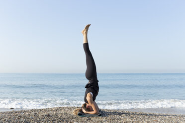 Junge Frau übt Yoga am Strand, macht Kopfstand - JPTF00124