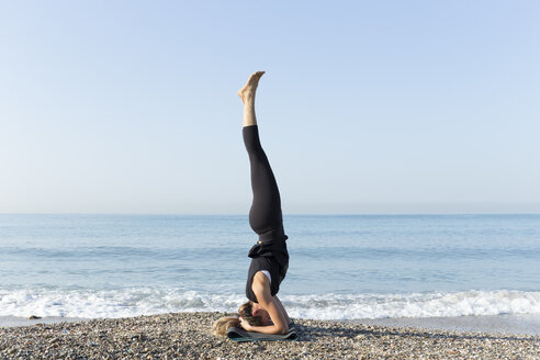 Young woman practicing yoga on the beach, doing headstand - JPTF00124