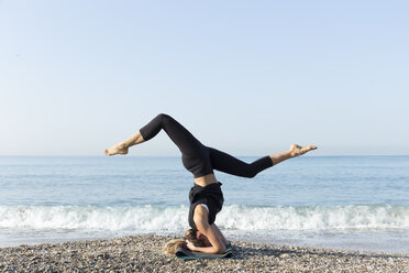 Junge Frau übt Yoga am Strand, macht Kopfstand - JPTF00125