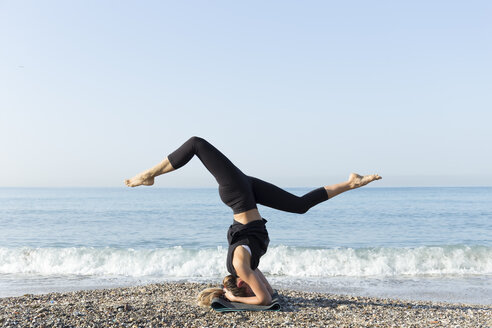 Young woman practicing yoga on the beach, doing headstand - JPTF00125