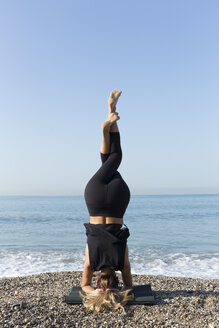 Young woman practicing yoga on the beach, doing headstand - JPTF00126