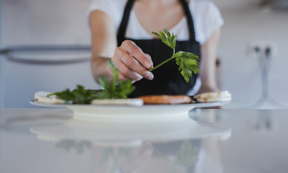 Die Hand einer jungen Frau garniert einen Teller mit vegetarischen Speisen, Nahaufnahme - LJF00085