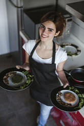 Portrait of smiling young woman holding garnished plates with vegetarian fritters - LJF00089
