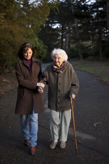 Frau geht mit ihrer Mutter auf einem gepflasterten Weg spazieren - BLEF05766