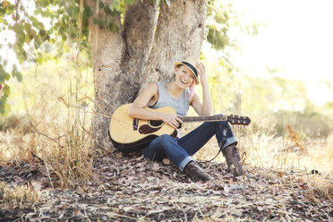 Caucasian musician holding guitar under tree - BLEF05807