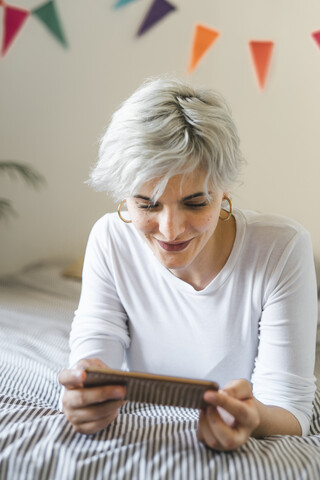 Lächelnde Frau mit Handy auf dem Bett zu Hause, lizenzfreies Stockfoto