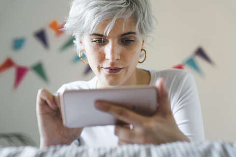 Frau benutzt Mobiltelefon auf dem Bett zu Hause, lizenzfreies Stockfoto