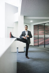 Geschäftsmann mit einer Tasse Kaffee auf einem Bein stehend im Büro - MOEF02174
