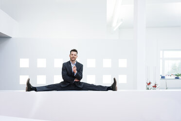 Smiling businessman doing the splits on reception desk in office - MOEF02188