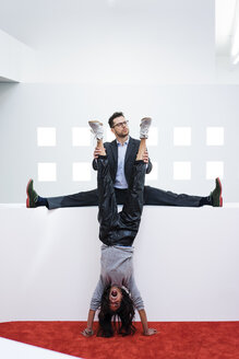 Businessman in office holding woman's legs doing a handstand - MOEF02190