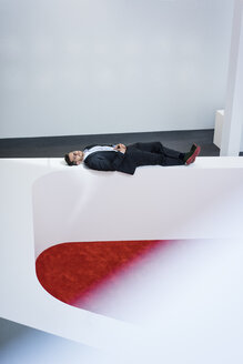 Businessman lying on reception desk in office - MOEF02191