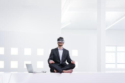 Businessman wearing VR glasses in office next to laptop - MOEF02202