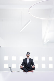 Businessman wearing VR glasses in office next to laptop - MOEF02204