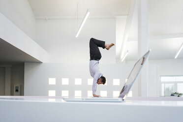 Geschäftsmann macht einen Handstand am Laptop im Büro - MOEF02210