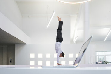 Geschäftsmann macht einen Handstand am Laptop im Büro - MOEF02211