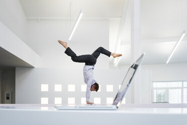 Geschäftsmann macht einen Handstand am Laptop im Büro - MOEF02212