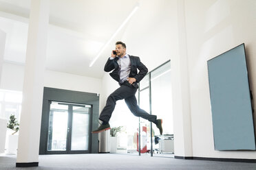 Businessman on cell phone jumping in office - MOEF02213