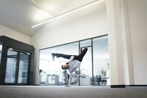 Businessman with cell phone doing a one-handed handstand on office floor - MOEF02216