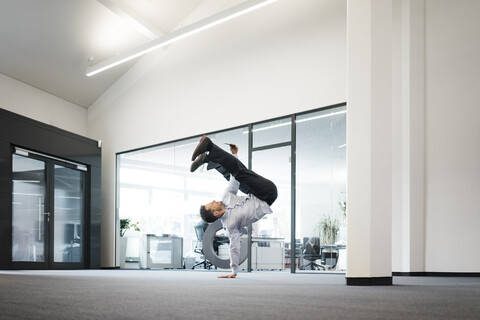 Geschäftsmann mit Mobiltelefon macht einen einhändigen Handstand auf dem Büroboden, lizenzfreies Stockfoto