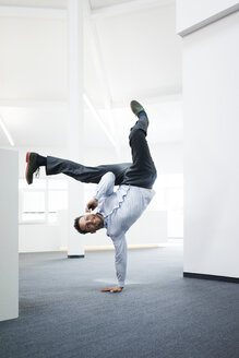 Geschäftsmann mit Mobiltelefon macht einen einhändigen Handstand auf dem Büroboden - MOEF02219