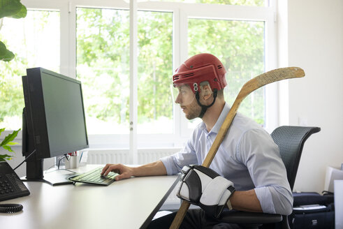 Als Eishockeyspieler verkleideter Geschäftsmann arbeitet am Schreibtisch im Büro - MOEF02227