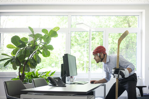 Als Eishockeyspieler verkleideter Geschäftsmann arbeitet am Schreibtisch im Büro - MOEF02228