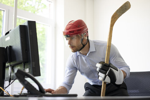 Als Eishockeyspieler verkleideter Geschäftsmann arbeitet am Schreibtisch im Büro - MOEF02229