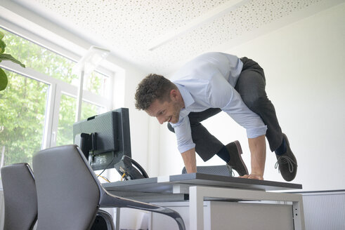 Businessman balancing on desk in office - MOEF02230