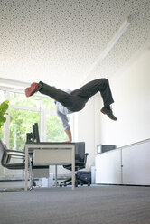 Businessman doing a one-handed handstand on desk in office - MOEF02234
