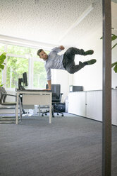 Businessman doing a one-handed handstand on desk in office - MOEF02235