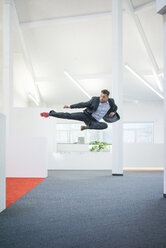Geschäftsmann springt in der Luft auf dem Büroboden - MOEF02238