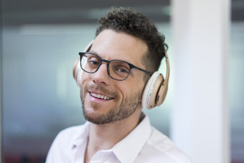 Porträt eines lächelnden Geschäftsmannes, der mit Kopfhörern Musik hört - MOEF02259
