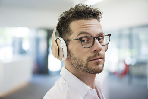 Portrait of businessman listening to music with headphones - MOEF02263