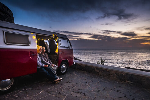 Älteres Paar, das in einem Oldtimer-Van unterwegs ist und den Sonnenuntergang am Meer beobachtet - SIPF01988