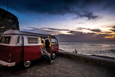 Älteres Paar, das in einem Oldtimer-Van unterwegs ist und den Sonnenuntergang am Meer beobachtet - SIPF01989