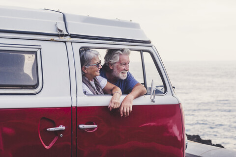 Senior couple traveling in a vintage van, looking at the sea stock photo