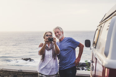 Senior couple traveling in a vintage van, taking pictures at the sea - SIPF02008