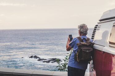 Senior man travelling in a vinatge van, using smartphone, rear view - SIPF02015