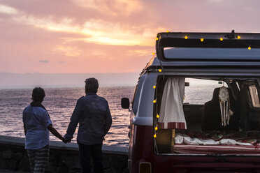 Senior couple traveling in a vintage van, watching sunset at the sea - SIPF02028