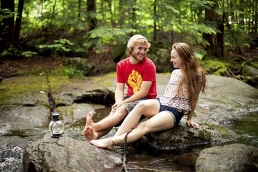 Couple sitting barefoot on boulders in forest - BLEF05869