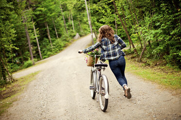 Rear view of girl pushing bicycle on dirt path - BLEF05899