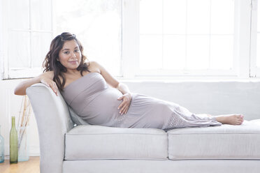 Schwangere hispanische Frau mit Bauch auf dem Sofa - BLEF06115