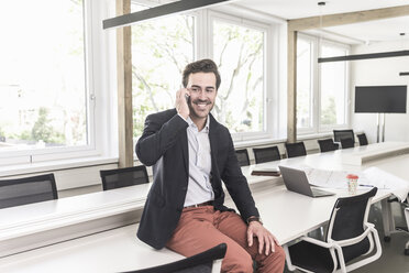 Young businessman sitting in boardroom, talking on the phone - UUF17687