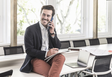 Young businessman sitting in boardroom, talking on the phone - UUF17694