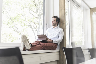 Young businessman sitting on windowsill, using digital tablet - UUF17701