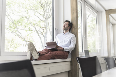 Young businessman with digital tablet sitting on windowsill, taking a break - UUF17702