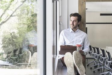 Young businessman sitting on windowsill, using digital tablet - UUF17707