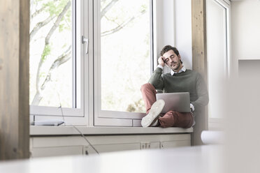 Young businessman with laptop sitting on windowsill, taking a break - UUF17713