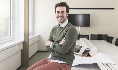 Successful, young businessman sitting in boardroom with arms crossed - UUF17729